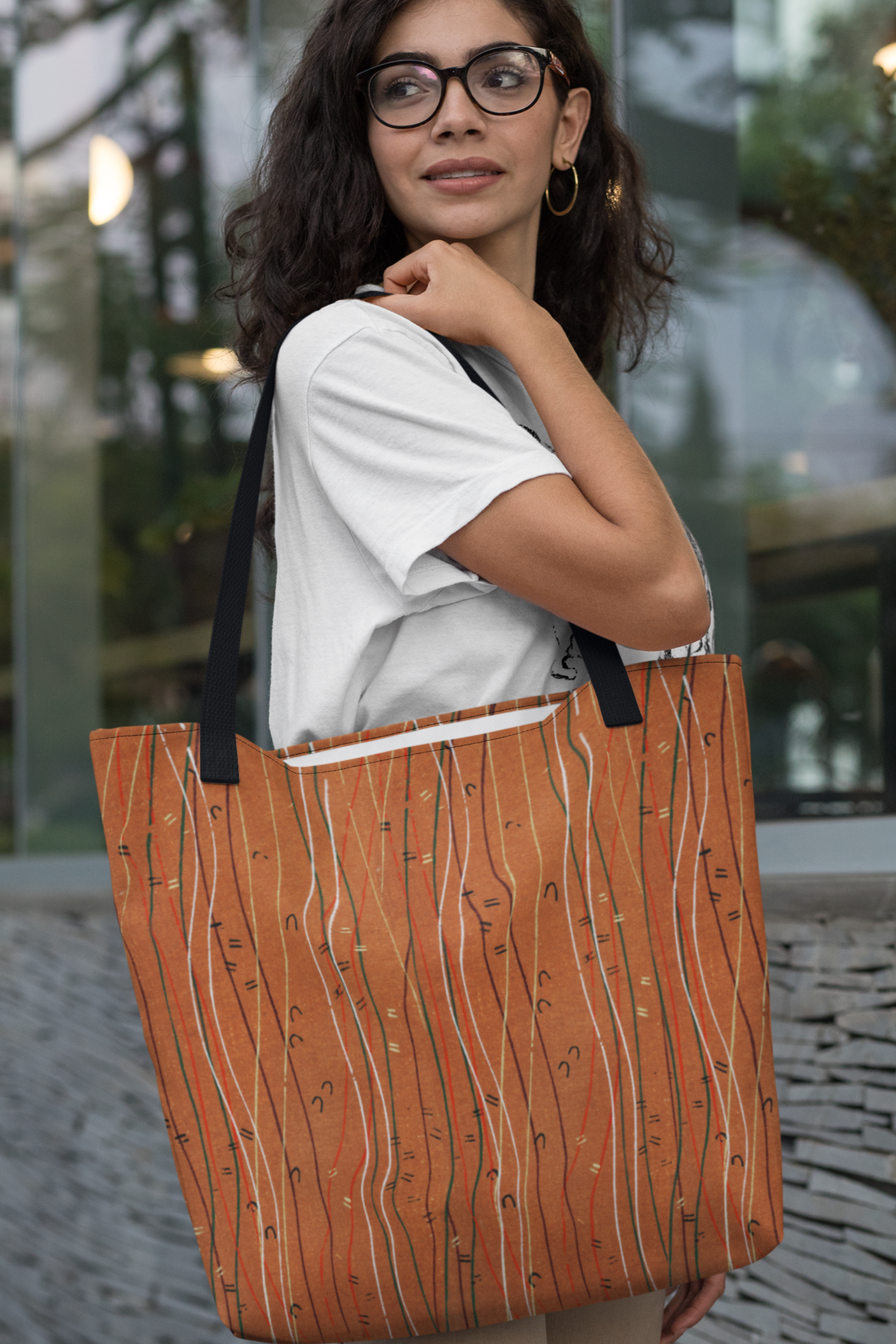 Woman holding an orange tote bag with a wavy pattern in an outdoor setting.