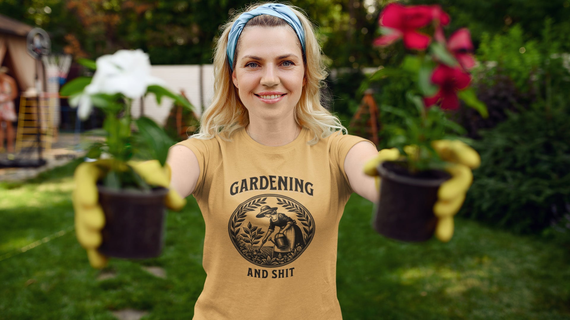 Person wearing a tan t-shirt with 'Gardening and Shit' text, holding potted plants in a garden setting.