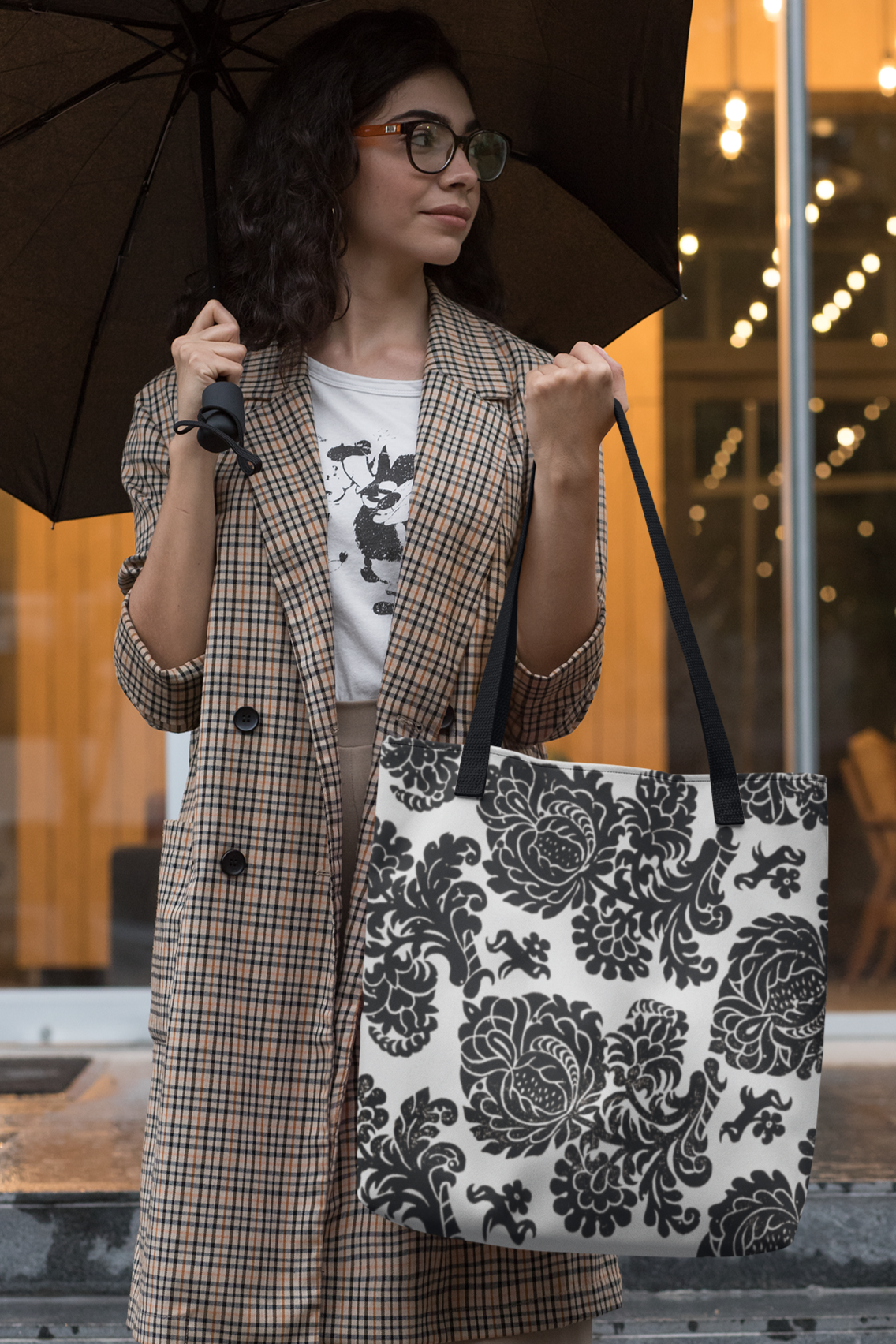Woman holding an umbrella and black and white floral pattern tote bag on a rainy day
